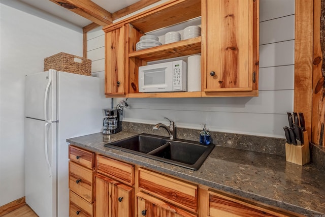 kitchen with brown cabinets, open shelves, a sink, dark stone counters, and white appliances