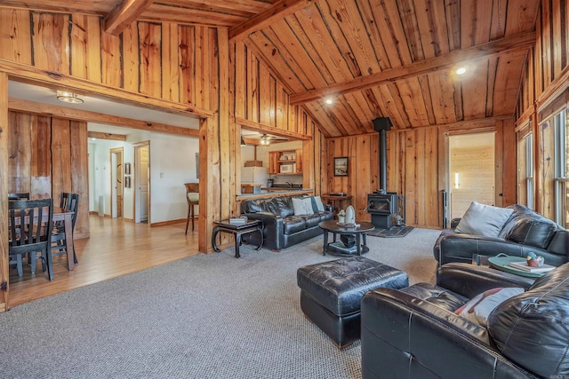 carpeted living room featuring a wood stove, wood walls, wooden ceiling, and beamed ceiling