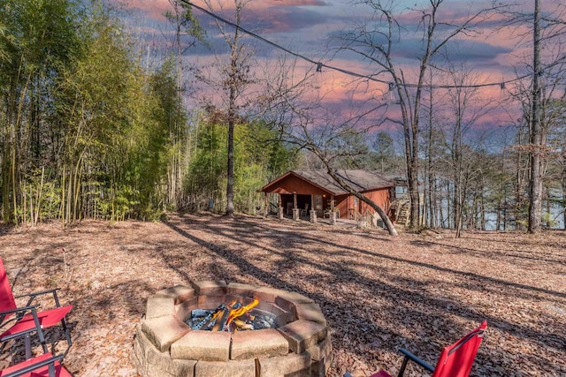 yard at dusk featuring a fire pit, a view of trees, and an outdoor structure