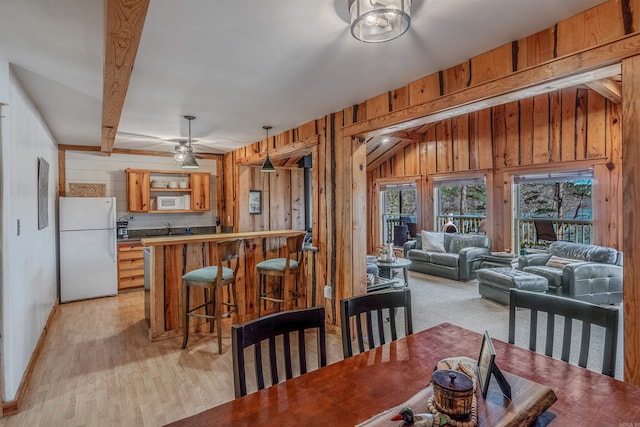 dining area featuring beamed ceiling, wood walls, bar area, and light wood-style floors