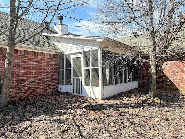 view of side of home with roof with shingles, brick siding, a chimney, and a sunroom