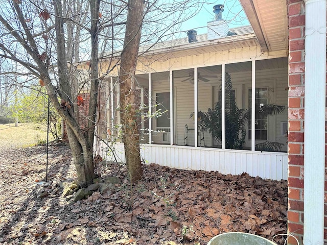 view of property exterior featuring a sunroom, a chimney, and brick siding