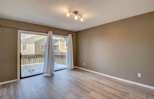 spare room featuring light wood-style floors, a textured ceiling, and baseboards