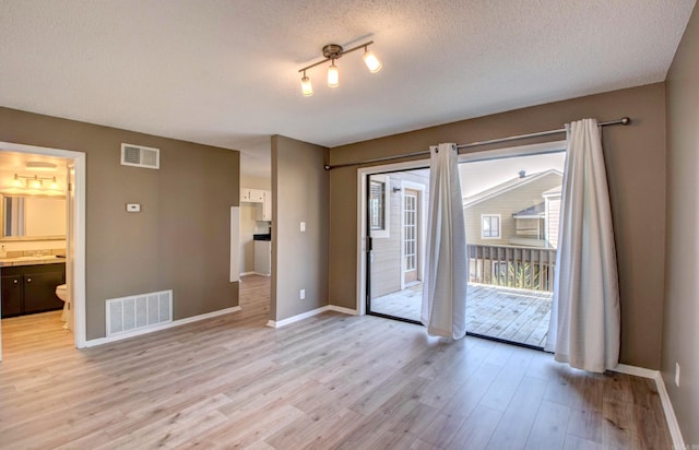 empty room with a textured ceiling, light wood-type flooring, visible vents, and baseboards