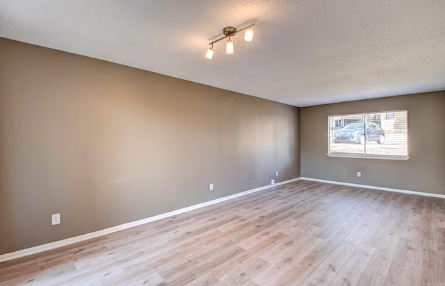 unfurnished room with light wood finished floors, baseboards, and a textured ceiling