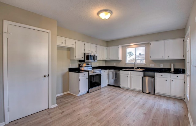 kitchen with a sink, white cabinetry, appliances with stainless steel finishes, light wood finished floors, and dark countertops