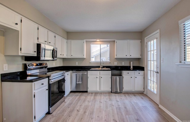 kitchen with appliances with stainless steel finishes, dark countertops, a sink, and white cabinetry