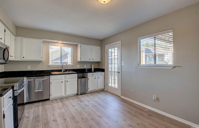 kitchen with stainless steel appliances, dark countertops, a sink, and white cabinetry