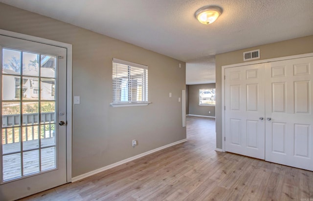 interior space with a textured ceiling, light wood-style flooring, visible vents, and baseboards