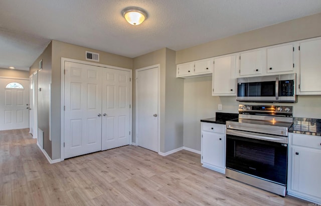 kitchen with dark countertops, visible vents, light wood-style flooring, appliances with stainless steel finishes, and white cabinetry