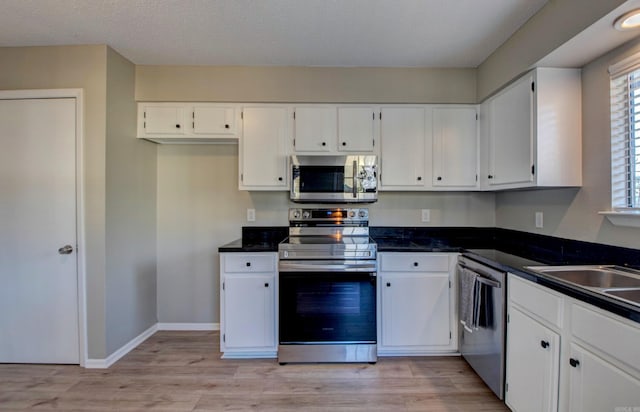 kitchen featuring dark countertops, light wood-type flooring, white cabinets, and stainless steel appliances