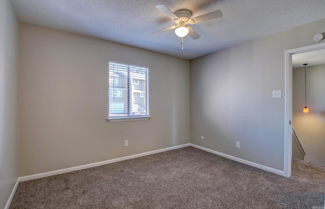 carpeted empty room with a textured ceiling, a ceiling fan, and baseboards