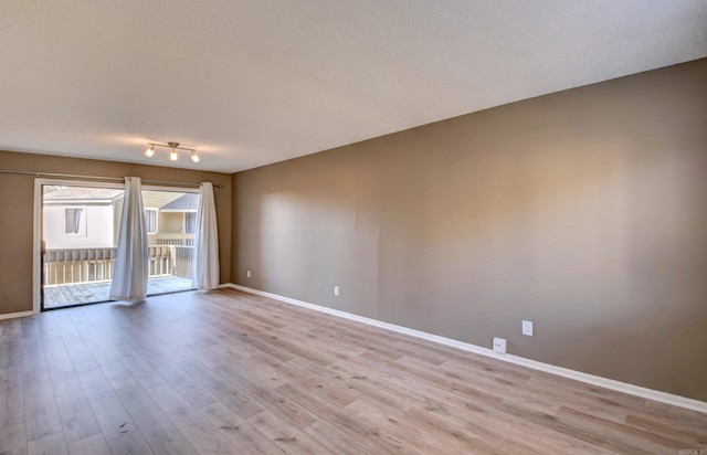 empty room with a textured ceiling, light wood-type flooring, and baseboards