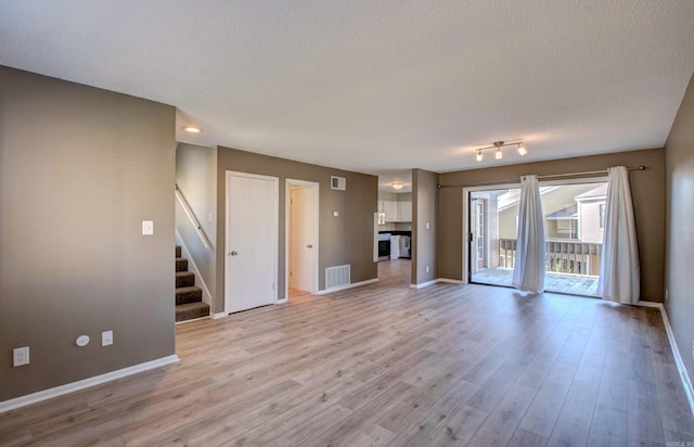 unfurnished living room featuring light wood finished floors, stairway, and visible vents