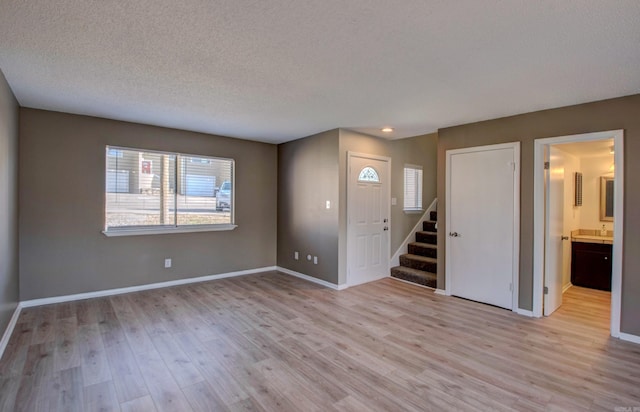 spare room featuring baseboards, stairway, a textured ceiling, light wood-type flooring, and a sink