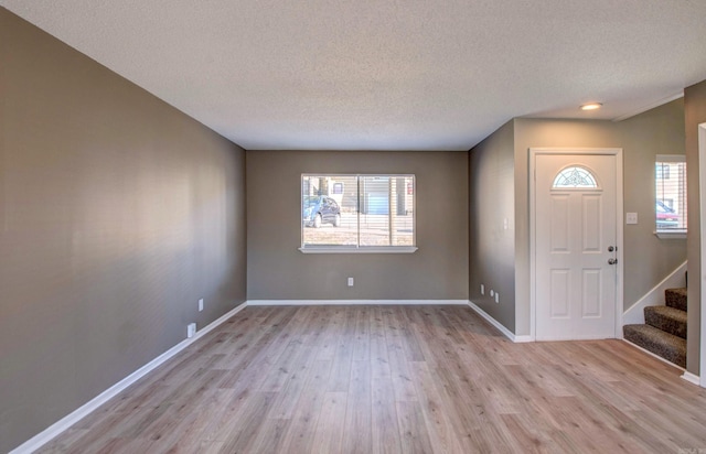 foyer entrance featuring light wood-type flooring, baseboards, stairway, and a textured ceiling