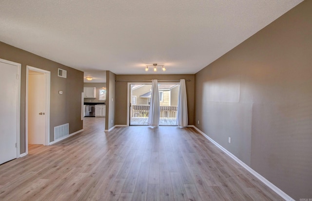 unfurnished living room featuring a textured ceiling, light wood-type flooring, visible vents, and baseboards