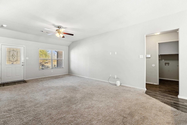 unfurnished living room featuring ceiling fan, vaulted ceiling, baseboards, and dark colored carpet