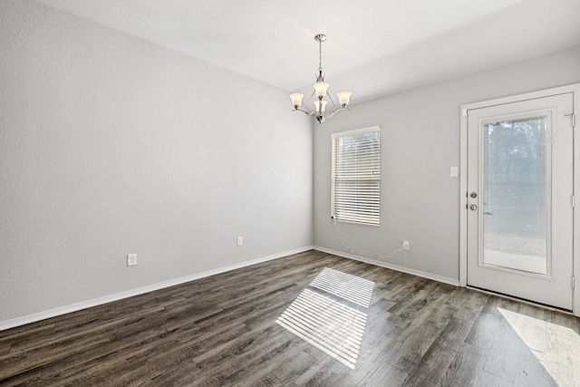 empty room with dark wood-type flooring, baseboards, and an inviting chandelier