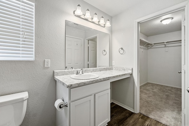 bathroom featuring a textured wall, wood finished floors, vanity, baseboards, and a spacious closet