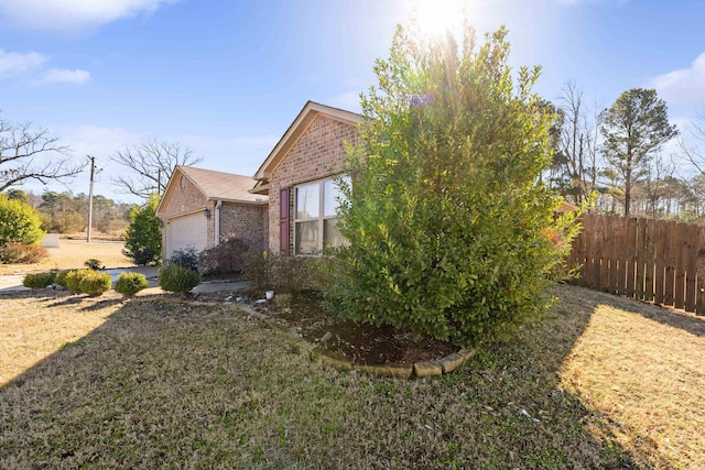 view of side of home with a garage, fence, a lawn, and brick siding