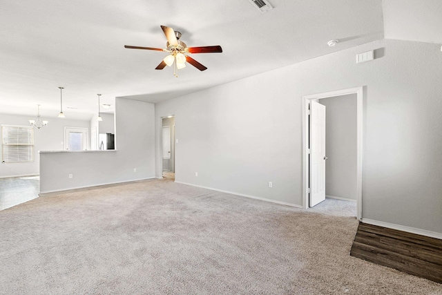 unfurnished living room with light colored carpet, visible vents, baseboards, and ceiling fan with notable chandelier