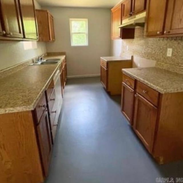 kitchen featuring tasteful backsplash, brown cabinets, light countertops, under cabinet range hood, and a sink