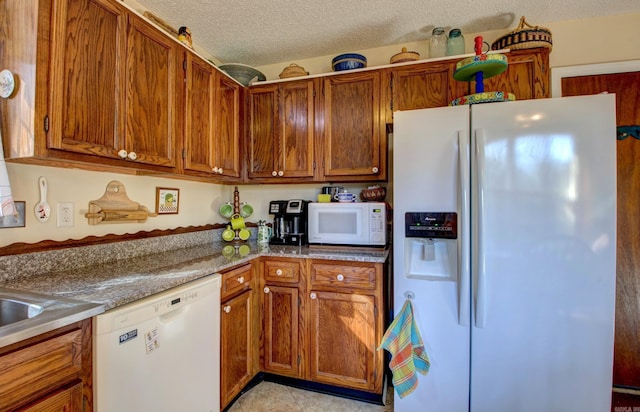 kitchen featuring light stone countertops, white appliances, brown cabinetry, and a textured ceiling