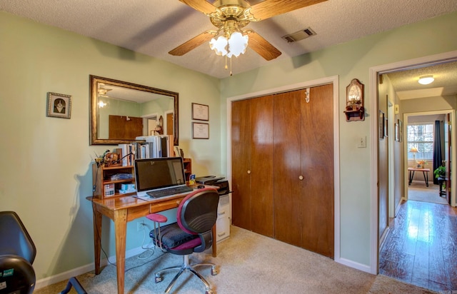 office featuring baseboards, visible vents, light colored carpet, ceiling fan, and a textured ceiling