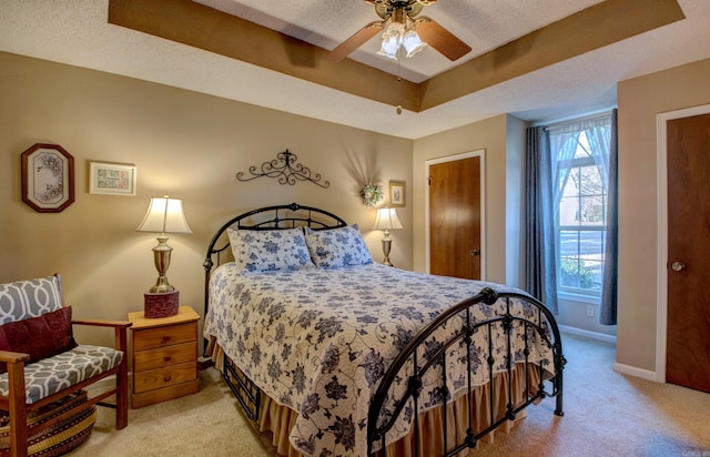 bedroom with light carpet, baseboards, ceiling fan, a tray ceiling, and a textured ceiling