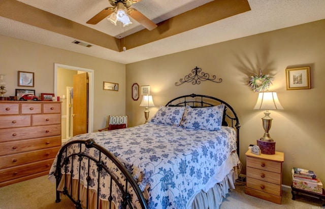 bedroom with a tray ceiling, visible vents, light carpet, and a textured ceiling