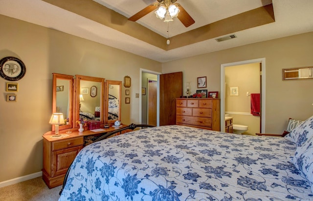 bedroom with baseboards, visible vents, light colored carpet, ensuite bathroom, and a tray ceiling