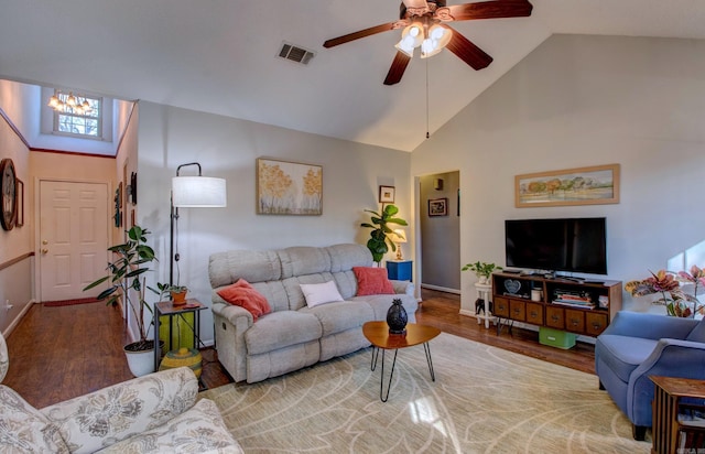 living area with ceiling fan with notable chandelier, high vaulted ceiling, wood finished floors, and visible vents