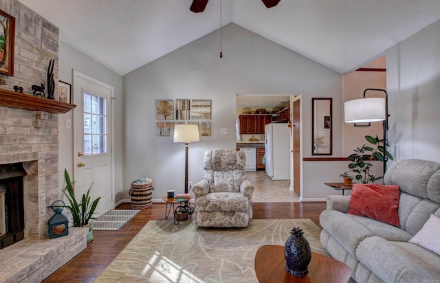 living area featuring wood finished floors, a ceiling fan, baseboards, vaulted ceiling, and a brick fireplace