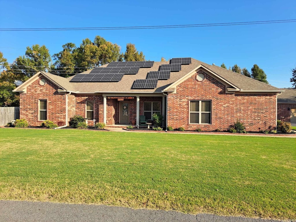 view of front of property with solar panels, brick siding, fence, roof with shingles, and a front lawn