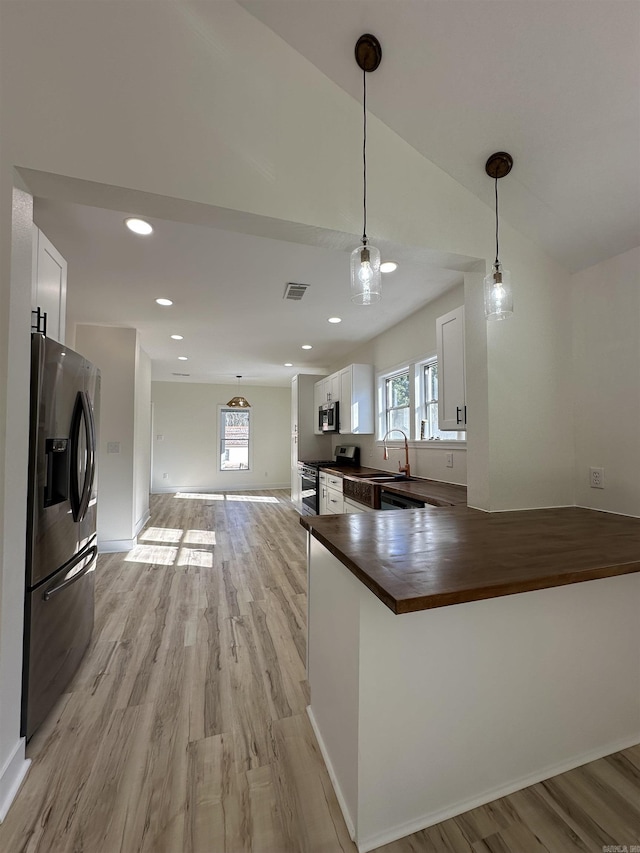 kitchen featuring light wood finished floors, white cabinets, decorative light fixtures, stainless steel appliances, and wooden counters