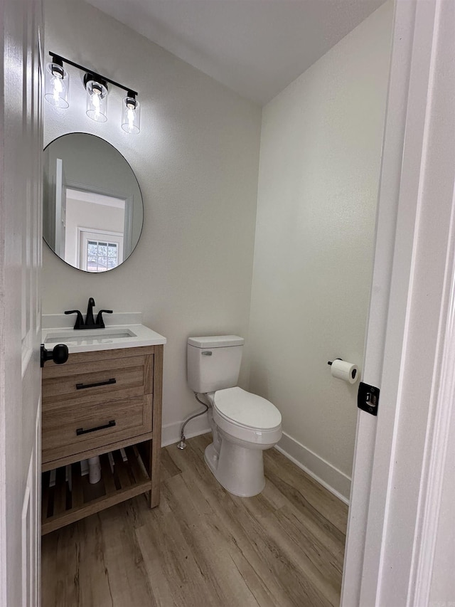 half bath featuring baseboards, vanity, toilet, and wood finished floors