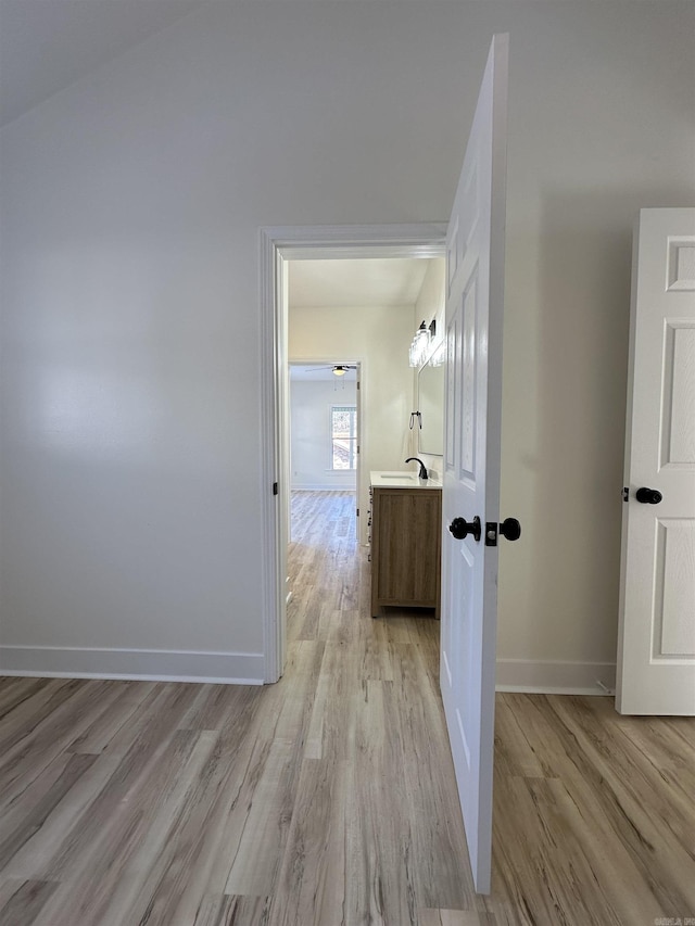 hallway with a sink, light wood-style flooring, and baseboards