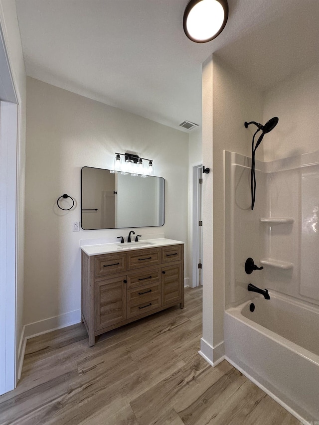 bathroom with wood finished floors, vanity, visible vents, baseboards, and tub / shower combination