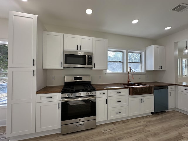 kitchen featuring a sink, visible vents, white cabinets, appliances with stainless steel finishes, and light wood finished floors