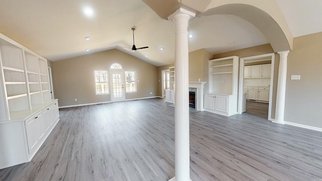 unfurnished living room featuring ceiling fan, a high end fireplace, light wood-style floors, vaulted ceiling, and ornate columns