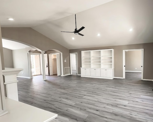 unfurnished living room featuring arched walkways, ceiling fan, wood finished floors, vaulted ceiling, and ornate columns