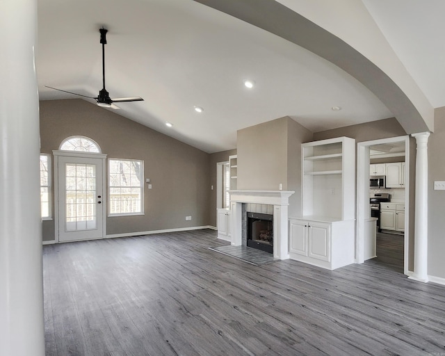 unfurnished living room with ceiling fan, light wood-type flooring, a tiled fireplace, and ornate columns