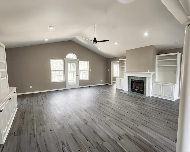 unfurnished living room with baseboards, a tiled fireplace, dark wood-style floors, ceiling fan, and vaulted ceiling