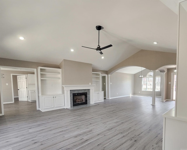 unfurnished living room with arched walkways, a ceiling fan, a tile fireplace, light wood-style flooring, and vaulted ceiling