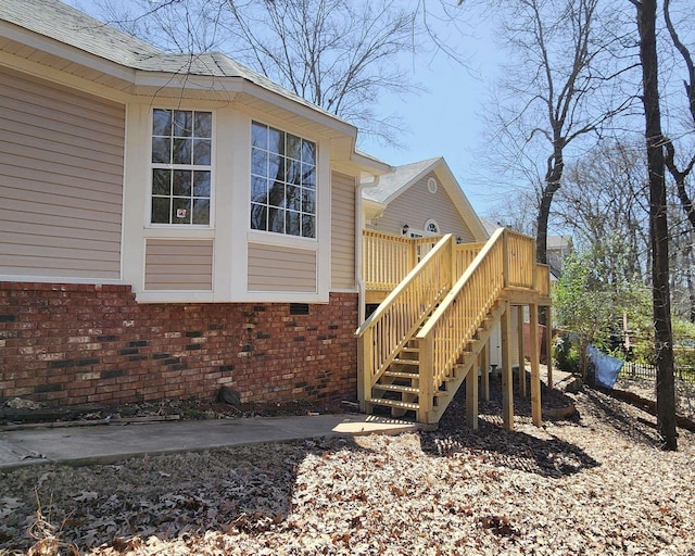 view of home's exterior featuring a wooden deck, stairway, roof with shingles, and brick siding