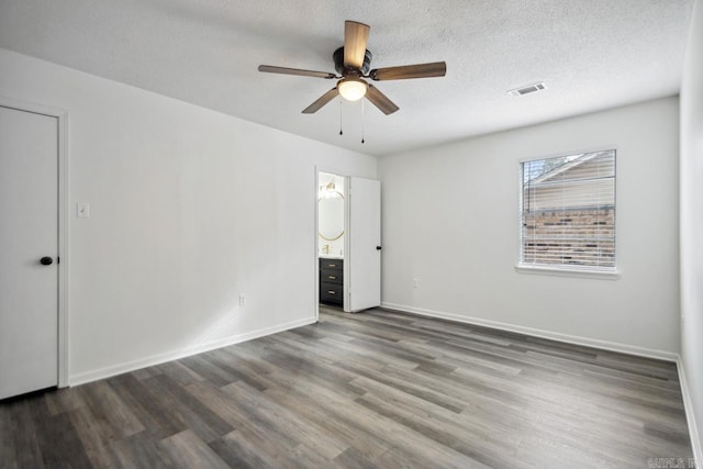 unfurnished bedroom with baseboards, visible vents, dark wood finished floors, ensuite bath, and a textured ceiling