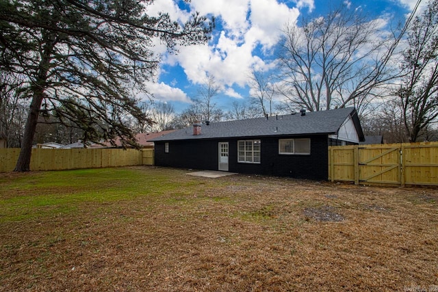 back of house featuring brick siding, a lawn, a fenced backyard, and a gate