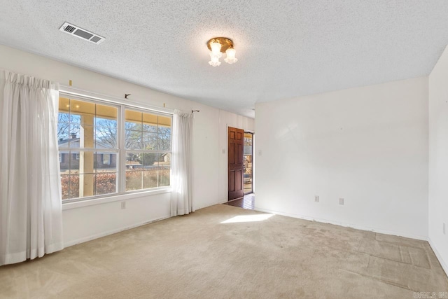 spare room with carpet, visible vents, and a textured ceiling