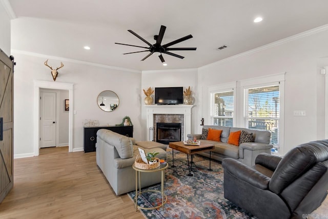 living room with light wood finished floors, a barn door, visible vents, a ceiling fan, and a tiled fireplace